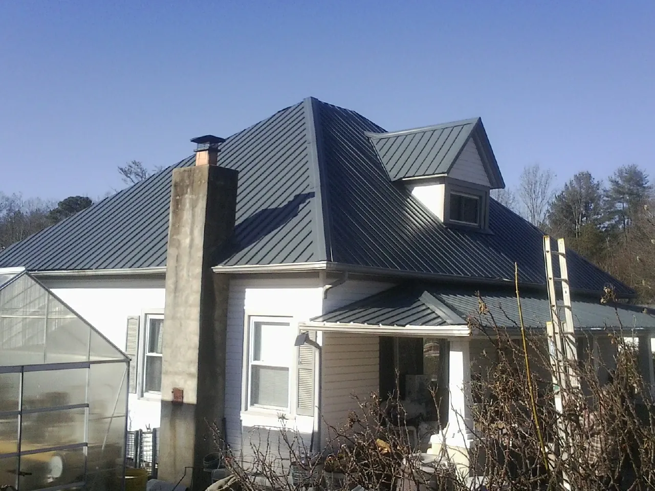 Dark blue standing seam metal roof on a white farmhouse with dormer — Slate & Tile Roof Repair by Roofing Brothers in East Freedom