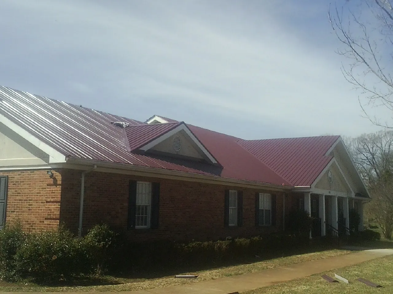 Red metal roof with gabled entries on a long brick building, from a Hail Damage Roof Repair job in East Freedom