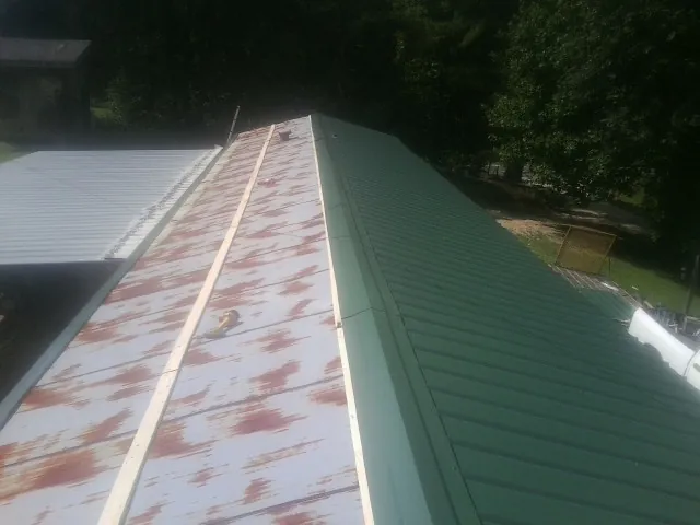 Old rusted panels beside newly installed green metal roofing — Wind Damage Roof Repair by Roofing Brothers in East Freedom