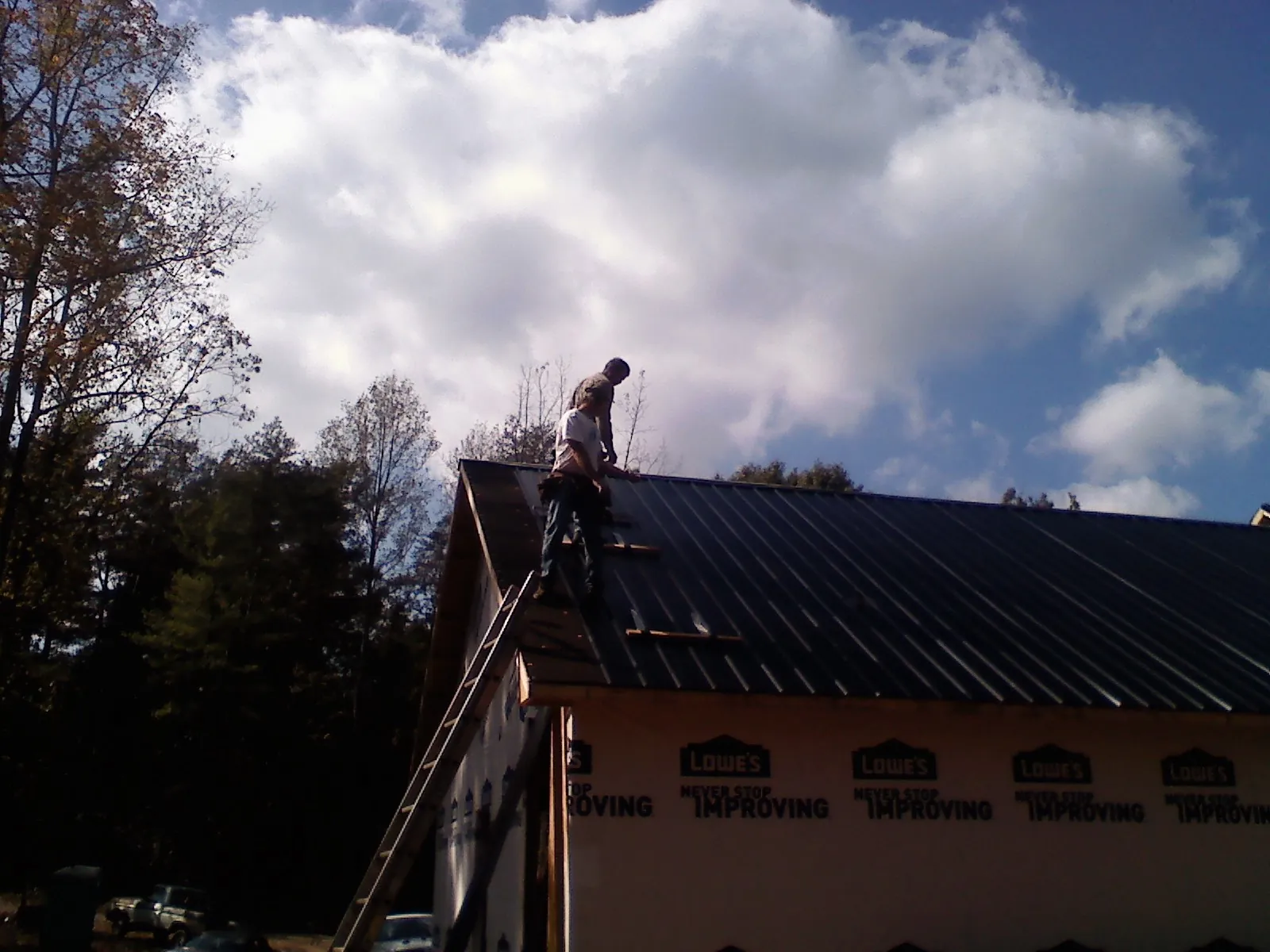 Roofer fastening dark metal panels high against a cloudy sky, from a Roof Inspection job in East Freedom