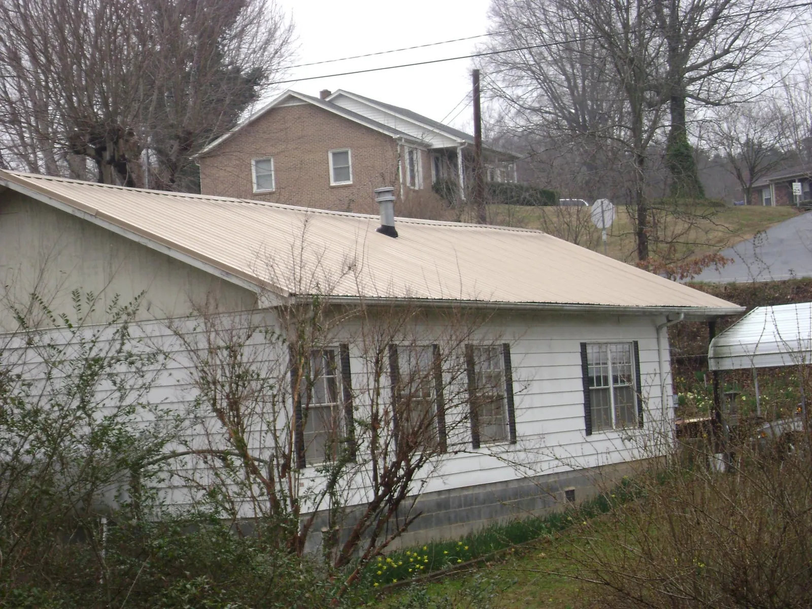 Tan metal roof on a white sided house set into a hillside — Commercial Roofing by Roofing Brothers in East Freedom