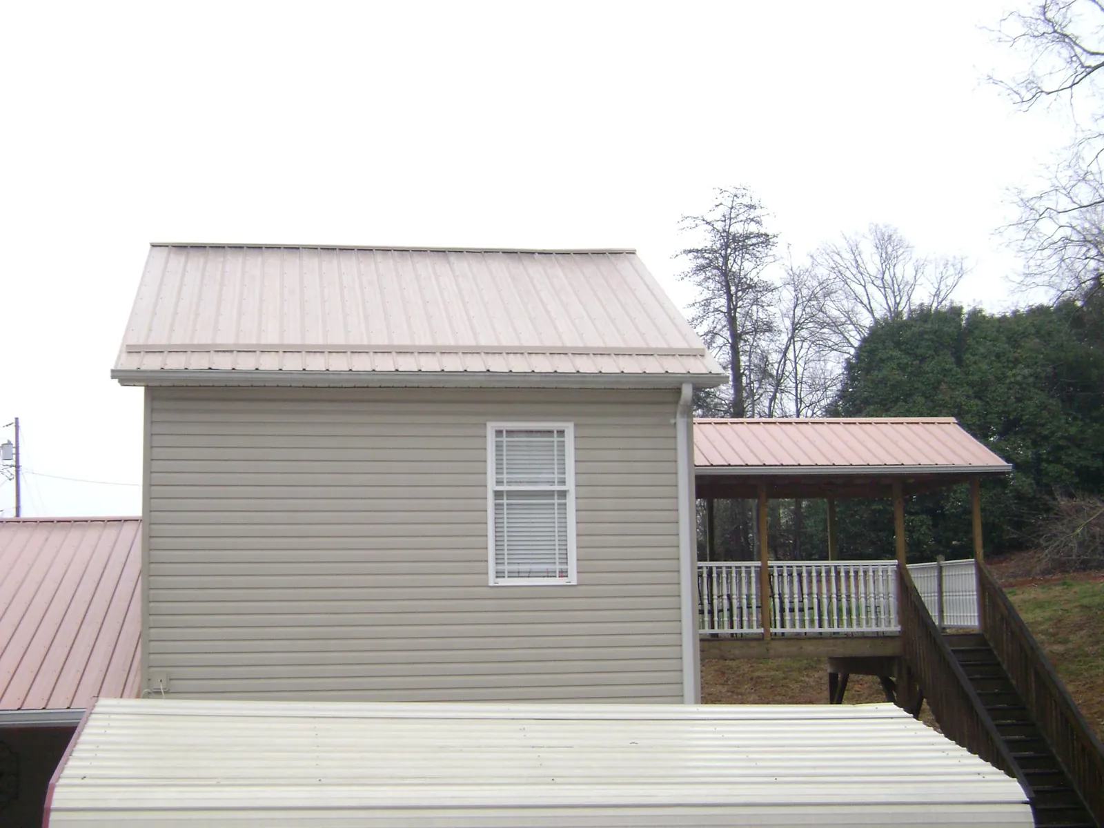 Tan metal roofs on a two story addition and attached porch, from a Roof Replacement job in East Freedom